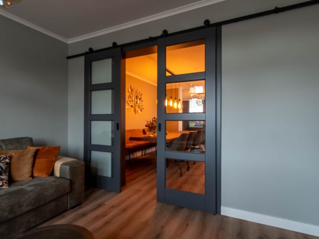 Maatwerk houten schuifdeuren met glas die twee ruimtes scheiden